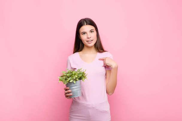 young pretty woman feeling happy, surprised and proud, pointing to self with an excited, amazed look with a plant - Photo, Image