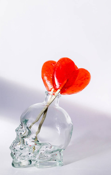 дві цукерки у формі серця стоять у глечику у формі черепа на білому тлі
 - Фото, зображення