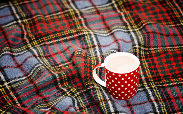 rot gepunktete Teetasse mit heißer Schokolade auf einer schottischen Decke. gemütliches Wohnkonzept mit rotem Porzellanbecher. eine Tasse festliche heiße Schokolade. traditionelle hausgemachte Weihnachtswerbung Kakao. Neujahr - Foto, Bild