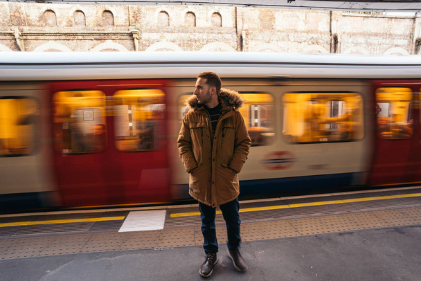 Lonely Young Handsome bearded man is waiting for train in subway station with blurry moving train in background. - 写真・画像