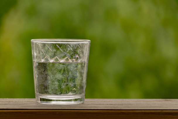 glass of water on a wooden table background of green bokeh - Photo, Image