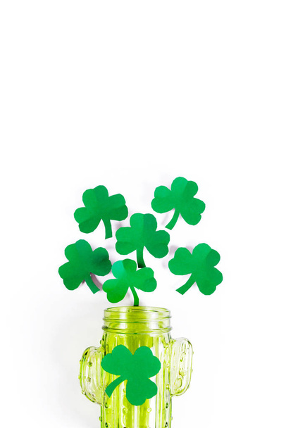 Green paper clover leaves spill out in the form of foam from a green glass - Фото, изображение
