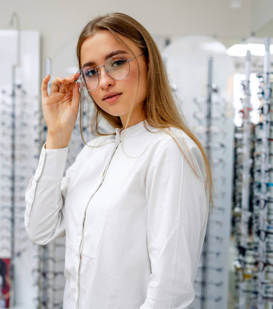 Eyeglasses closeup. Woman in spectacles. Choosing glasses. Client in optics. Selective focus. Woman in corrective glasses looking to the camera. Stand with spectacles. Wide assortment in shop. - Φωτογραφία, εικόνα
