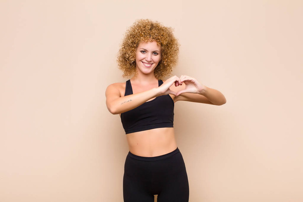 young afro woman smiling and feeling happy, cute, romantic and in love, making heart shape with both hands sport concept - Foto, Imagem