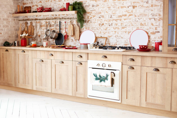 Modern konyhabútor téglafalon. Karácsonyi konyha belső. Skandináv dizájn. a konyha szervezése. Rusztikus konyha bútorokkal, fa munkalappal és sütővel, edények, tányérok. - Fotó, kép
