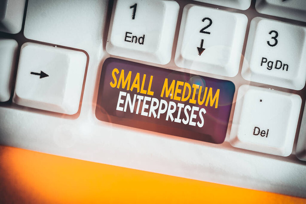 Küçük Medium Enterprises 'ı gösteren kavramsal el yazısı. Kavram, binlerce çalışanı olan şirketlerin beyaz arkaplanın üzerinde nota kağıtları olan beyaz bilgisayar klavyesi anlamına geliyor. - Fotoğraf, Görsel