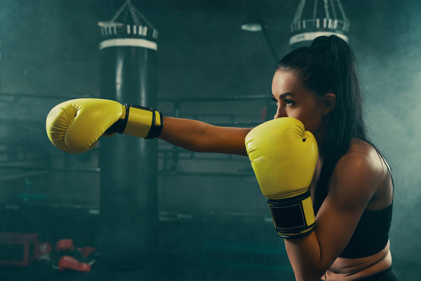 Action shot of young athletic woman training with punching bag wearing yellow boxing gloves - Foto, afbeelding