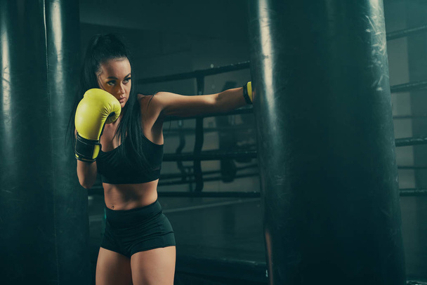 Strzał akcji młodej atletycznej kobiety trenującej z workiem bokserskim w żółtych rękawiczkach bokserskich - Zdjęcie, obraz