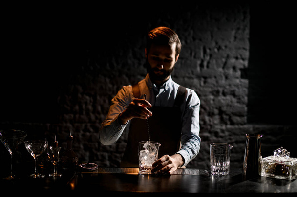 Professional male bartender stirring an ice cubes in the glass with special spoon to the glass - Foto, afbeelding
