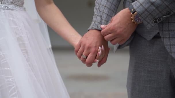 Milující šťastný manželský pár držící se zblízka za ruce. Pohledný ženich v kostkovaném obleku narovnává rukáv bundy a držet ruku mladé nevěsty v bílých krásných svatebních šatech v ranní venkovní. - Záběry, video