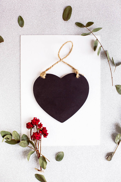 Background with copy space blank on table with black heart, eucalyptus branch, roses flowers and leafs. White paper top view, flat lay, minimal style. Moke up card. - Photo, Image