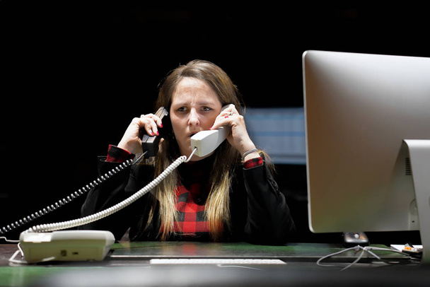 Mulher sentada em sua mesa trabalhando e respondendo a um telefonema
. - Foto, Imagem