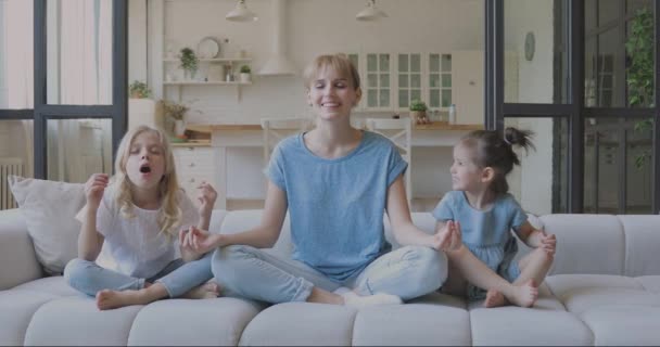 Happy young nanny teaching small girls yoga breathing exercises. - Video, Çekim
