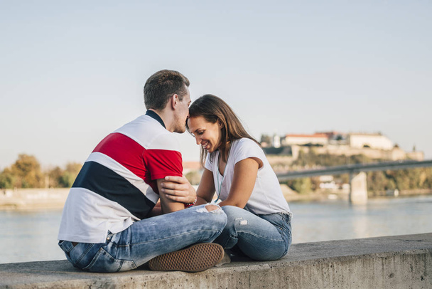 Couple in jeans sitting facing each other by the river - Foto, Imagen