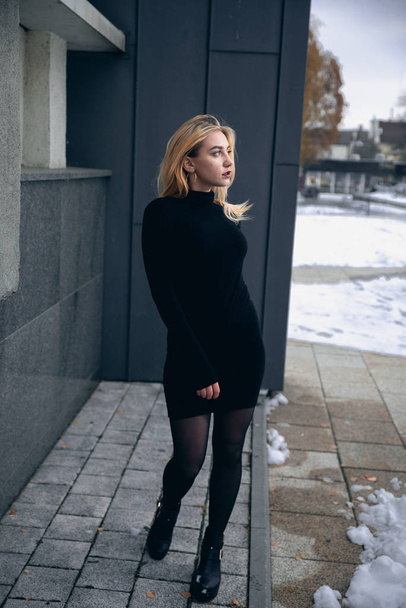 Girl in a black dress in the winter on a background of a dark building - Φωτογραφία, εικόνα