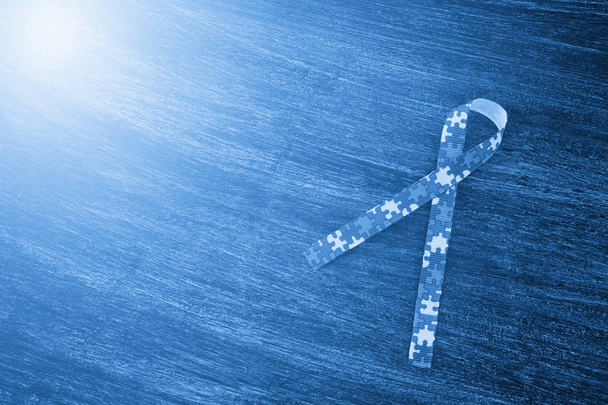 Wereld Autisme bewustzijn en trots dag of maand met Puzzel patroon lint op houten achtergrond. Blauw filter - Foto, afbeelding