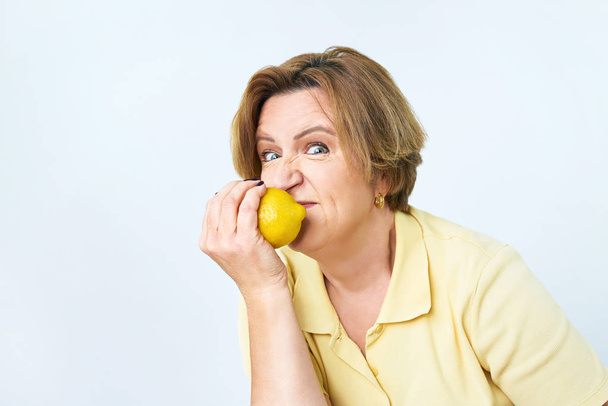 Starší žena s citrónem v ruce dělá funky akci. Starší žena jí citrón. Ona drží dietu. Ona hledá krásu a hubnutí. - Fotografie, Obrázek