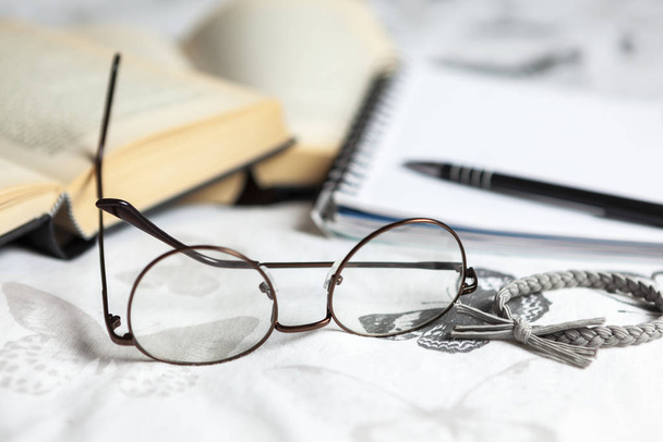 Coppia di occhiali da lettura e una fascia per capelli su un letto con alcuni libri
 - Foto, immagini