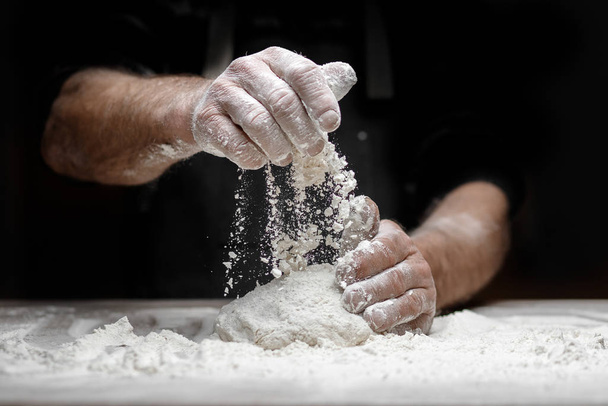 Férfi pék kezei élesztőtésztát készítenek fehér lisztporral fekete alapon, tésztát és pizzát készítenek - Fotó, kép