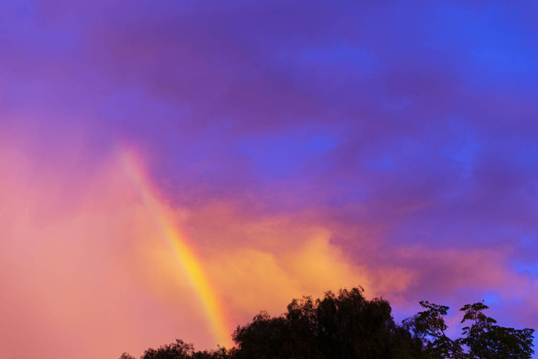 Sateenkaari leikkaa läpi auringonlaskun myrskypilvi liikkuvan yläpuolella
 - Valokuva, kuva