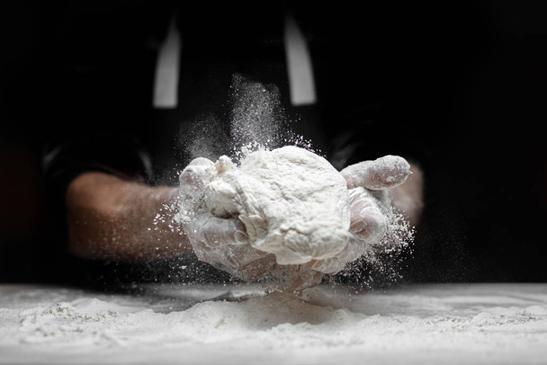 Hands baker preparing yeast dough with white dust flour on black background, scoop for pasta and pizza - Zdjęcie, obraz