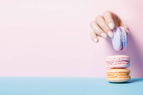 Девочка держит за руки печенье макарон. Стильный модный женский маникюр на розовом фоне, пространство для копирования
 - Фото, изображение