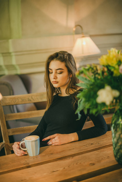 Beautiful elegant brunette girl wearing a black dress is relaxing in a street cafe. Advertising, fashion. Tinted photo - Фото, зображення