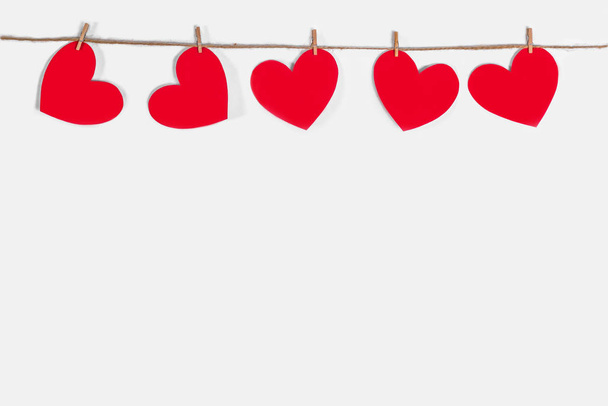Garland of red hearts on a white isolated background. Natural rope and clothespins. The concept of recognition in love, romantic relationships, Valentines Day. Copy space - Foto, imagen