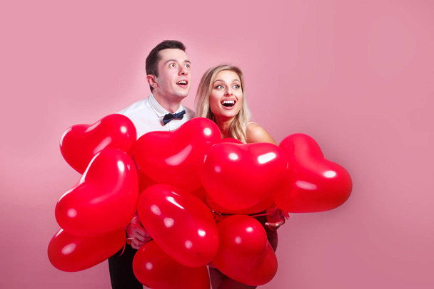 Funny surprised young couple with balloons heart on pink background - 写真・画像
