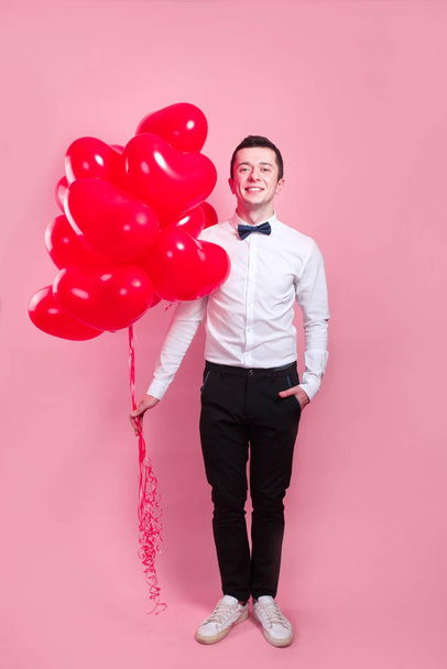 Яскравий молодий чоловік з повітряними кулями у формі серця на рожевому тлі. Людина у день святого Валентина. - Фото, зображення