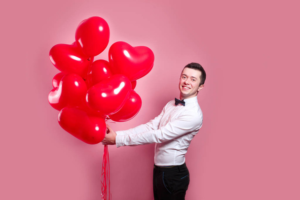 Elegant young man with heart shape air balloons on pink background. Valentines Day. - Fotó, kép