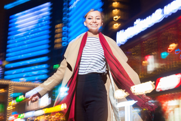 Cheerful girl in trendy apparel excited with night lights in Big City, beautiful brunette woman happy about spending evening free time in downtown with neon illumination. - Fotoğraf, Görsel