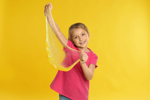Little girl with slime on yellow background - Foto, Imagen