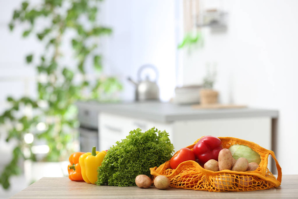 Net bags with vegetables on wooden table in kitchen - Foto, immagini