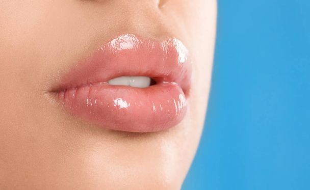 Young woman with beautiful full lips on light blue background, closeup - Foto, afbeelding