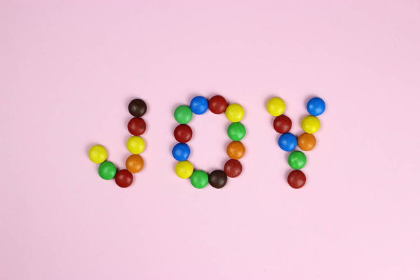 Word joy made of colored candies on a pink background - Photo, Image