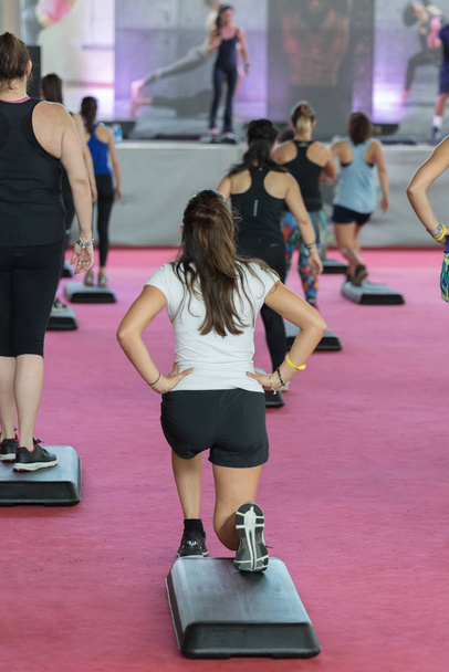 Entrenamiento Fitness en Gimnasio: Gente haciendo Ejercicios en Clase con Step Platform, Música y Profesora en el Escenario
 - Foto, Imagen