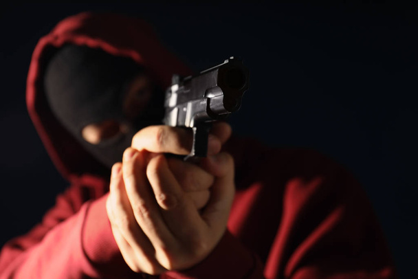 Man in mask holding gun on dark background, focus on hands - Fotografie, Obrázek