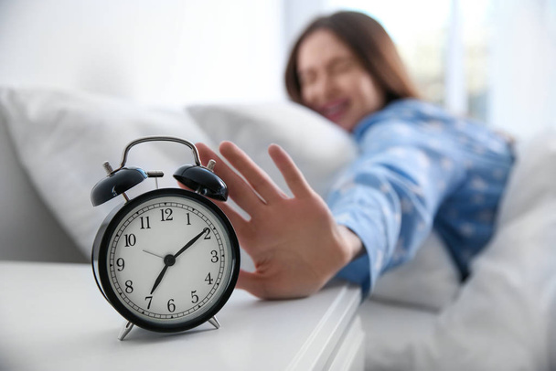 Young woman turning off alarm clock at home in morning, focus on hand - 写真・画像