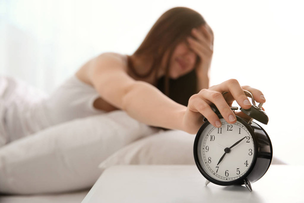 Young woman turning off alarm clock at home in morning, focus on hand - Fotoğraf, Görsel