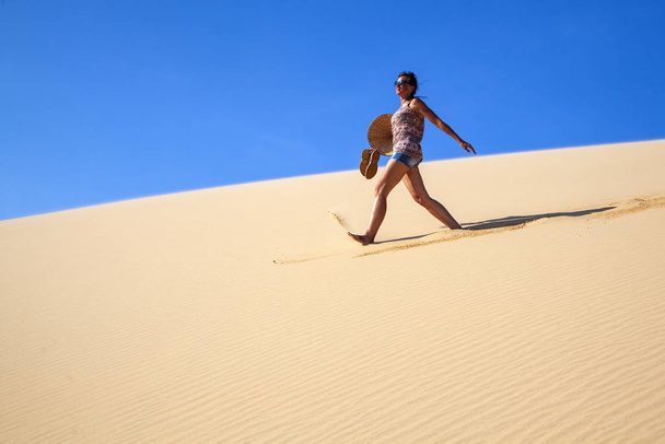 όμορφο κορίτσι στην έρημο πηγαίνει σε ένα λόφο ξυπόλητος στην άμμο - Φωτογραφία, εικόνα