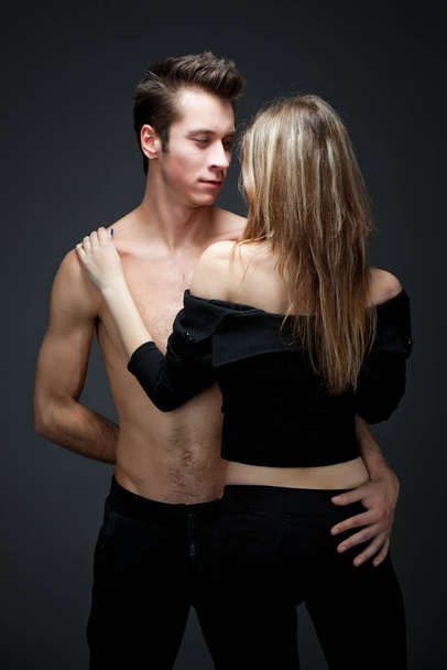 Young beautiful loving sexy couple standing and looking to each other over dark grey background - Foto, Imagem