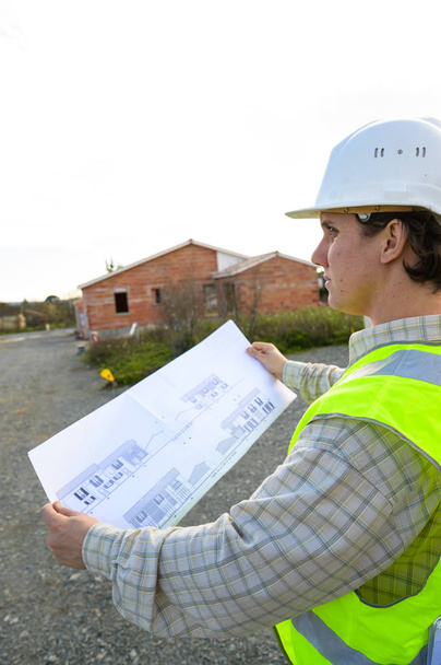 Professional engineer architect worker with protective helmet and blueprints paper at house building construction site background - Fotografie, Obrázek