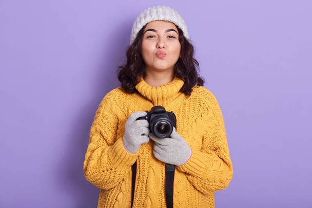 Portrait of charming lovely pretty young lady putting lips together, looking directly at camera, holding camera in both hands, photographer getting pleasure while taking photos. Hobby concept. - Фото, зображення