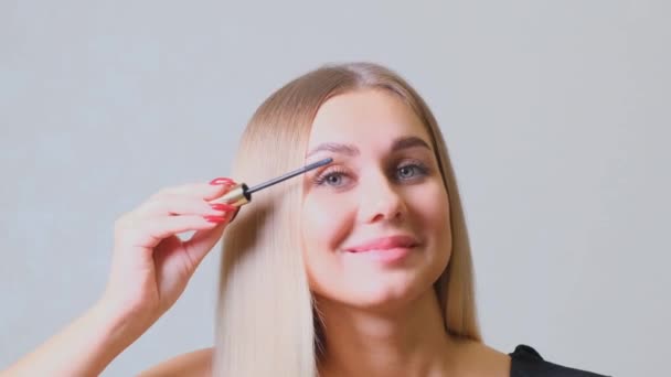 Ładna blondynka nakładająca makijaż na rzęsy przed lustrem. Piękno i makijaż koncepcja - Materiał filmowy, wideo