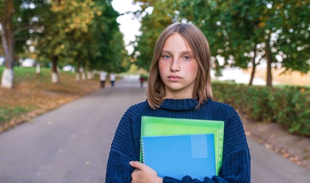 Sad and upset. A teenager girl of 12-15 years old, in summer in city, is holding notebooks and textbooks in her hands. Free space for copy text. The concept parenting thoughts of adolescents. - Fotó, kép