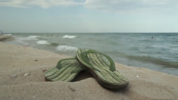 Akcesoria do plaży leżącej na piasku, męskie kapcie i okulary przeciwsłoneczne na piasku plaży - Materiał filmowy, wideo