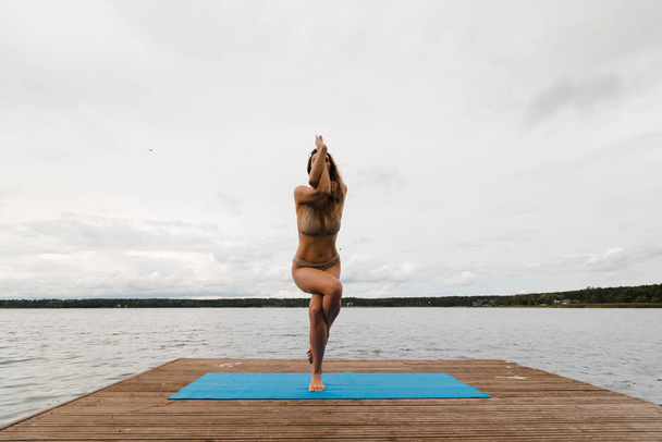 Fit femme mince pratiquant des exercices de yoga portant un mini maillot de bain bikini au lac avec des nuages - Yoga méditation et concept de style de vie de bien-être - Européenne Lettonie orientale Riga
 - Photo, image