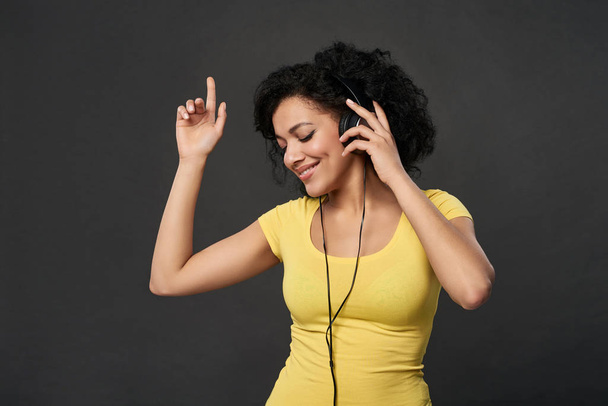 Happy woman listening music in headphones and dancing with closed eyes - Fotó, kép