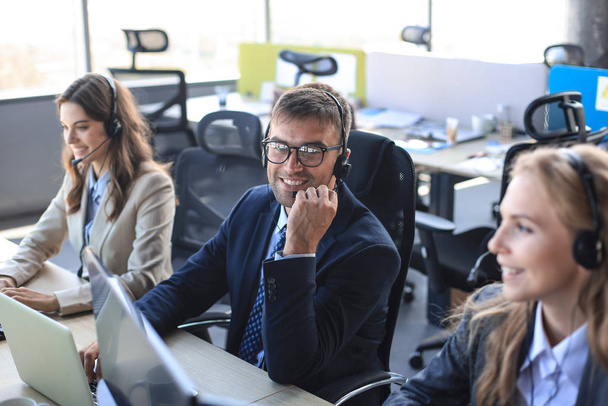 Portrait of call center worker accompanied by his team. Smiling customer support operator at work. - Φωτογραφία, εικόνα